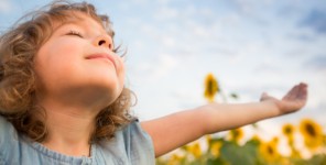 Glückliches Kind breitet die Arme aus im Sonnenblumenfeld